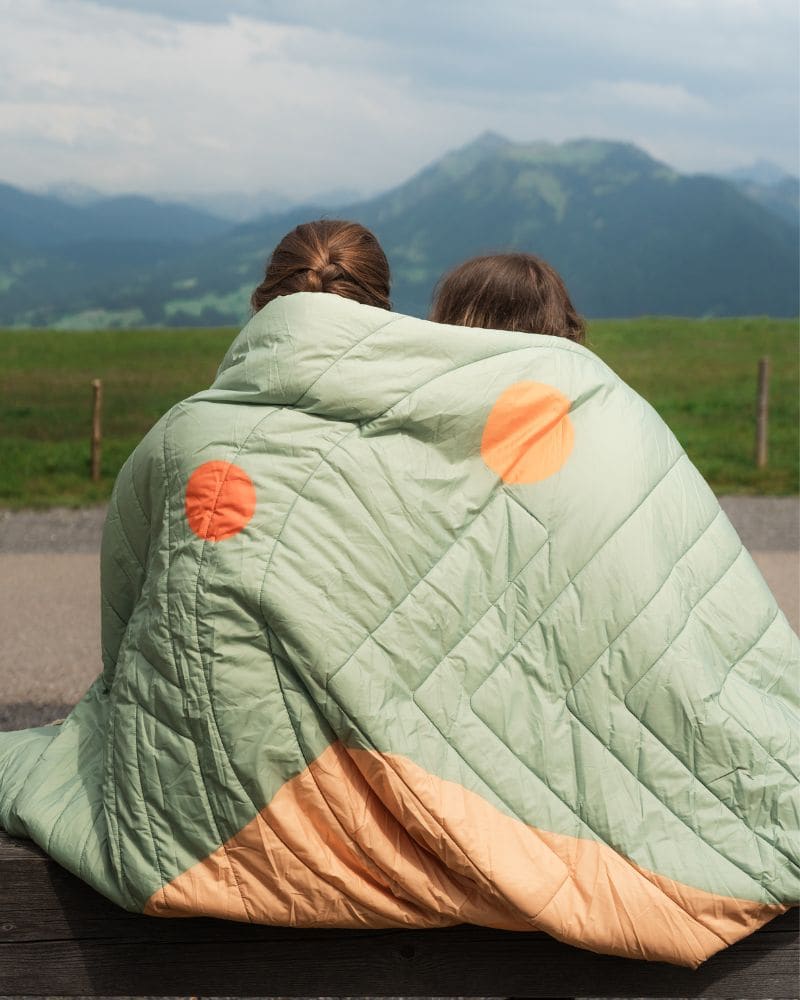 Two people sitting on a bench with a Queen Cloudtouch over them, looking at mountains.